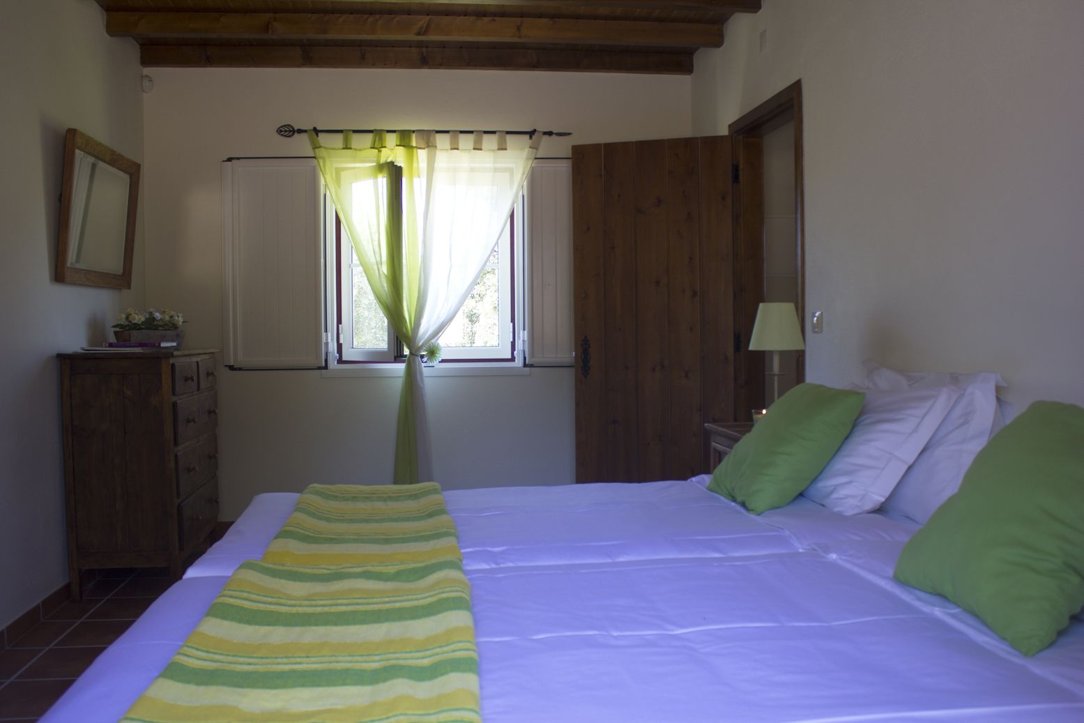 Un dormitorio con cama, ventana con cortinas, armario de madera y lámpara de noche.