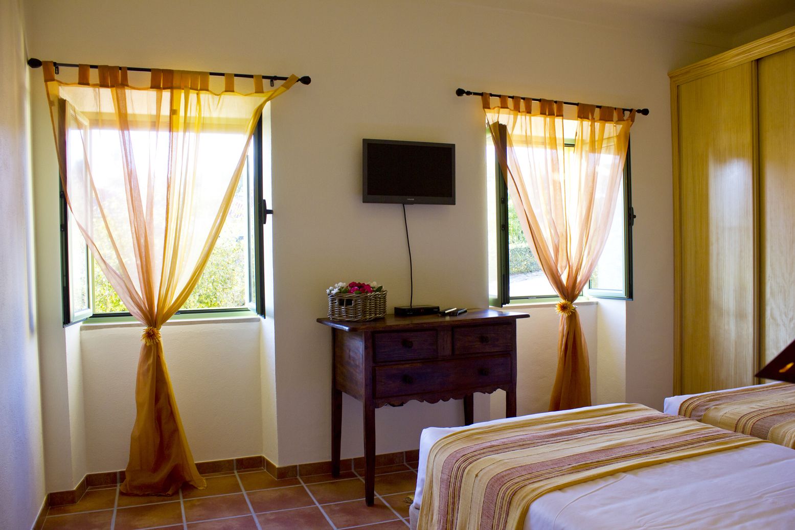 Camera d'albergo con due letti, una TV a parete e una scrivania con un cestino di fiori.