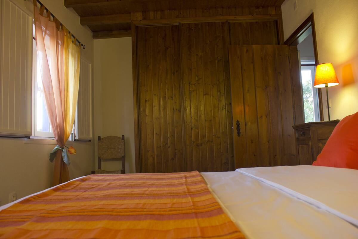 Quarto com cama, guarda-roupa de madeira e uma cadeira.