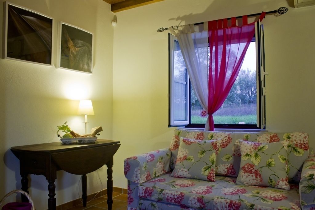 A room with a floral sofa, a table with a lamp, and a window with a curtain.