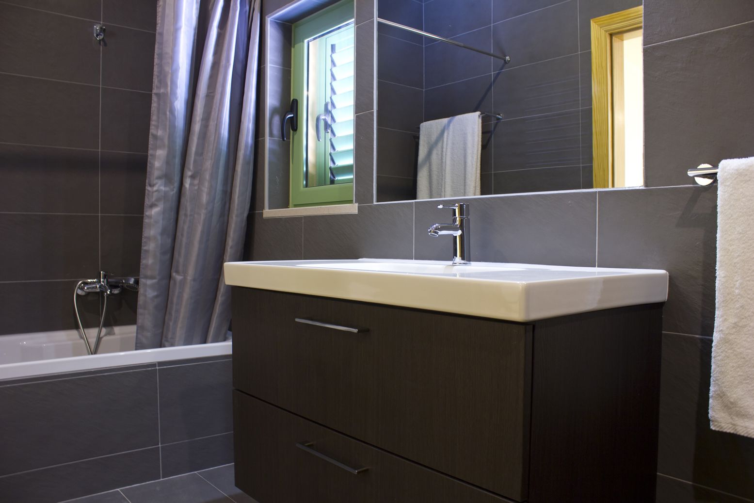 Ein modernes Badezimmer mit einer Badewanne, einem Waschbecken mit Spiegel darüber und einem Handtuch an der Wand.