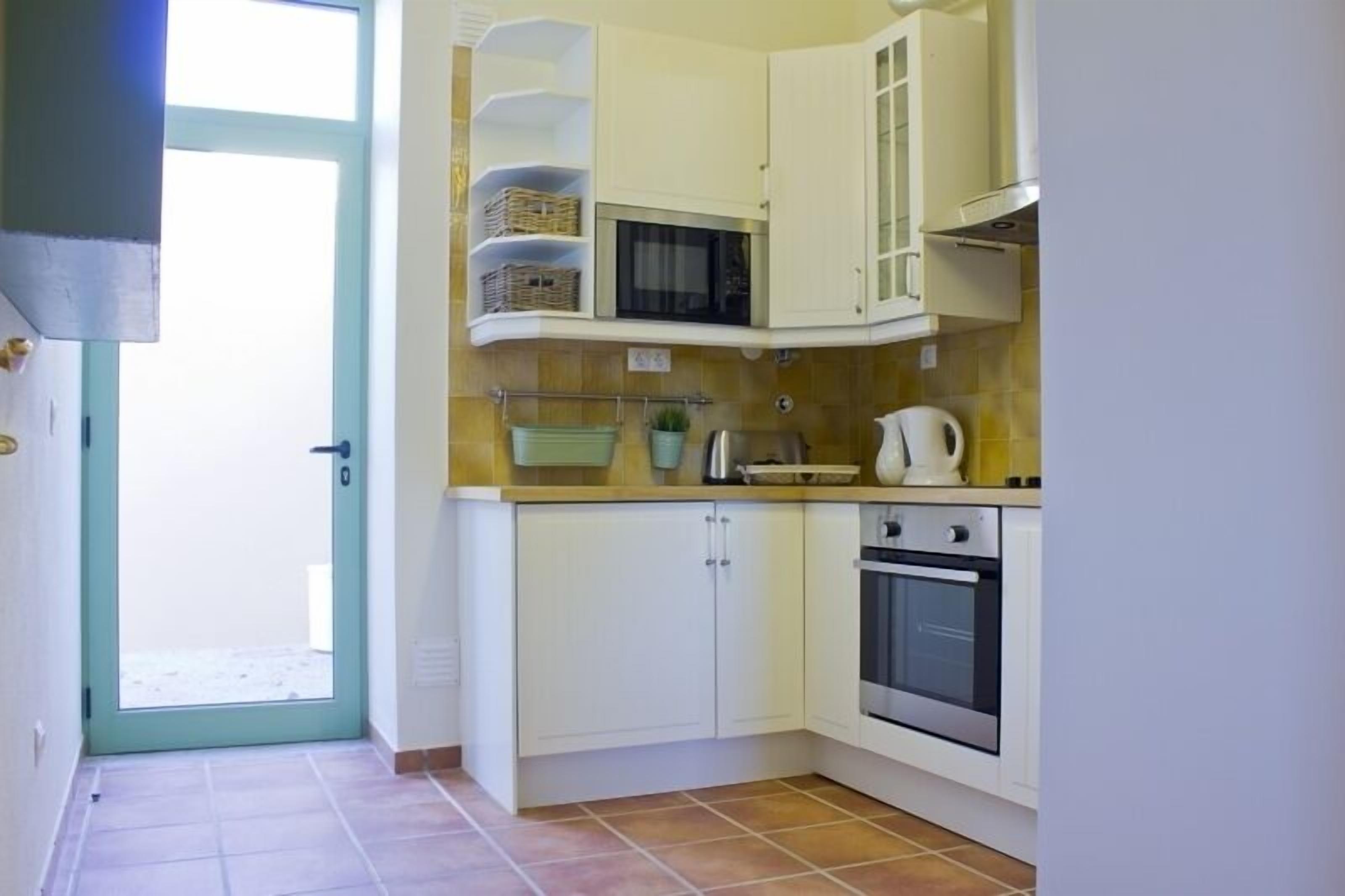 A compact kitchen with white cabinets, a microwave, a kettle, and a stove.