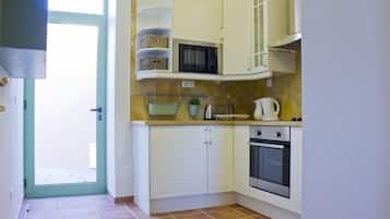 A compact kitchen with white cabinets, a microwave, a kettle, and a stove.