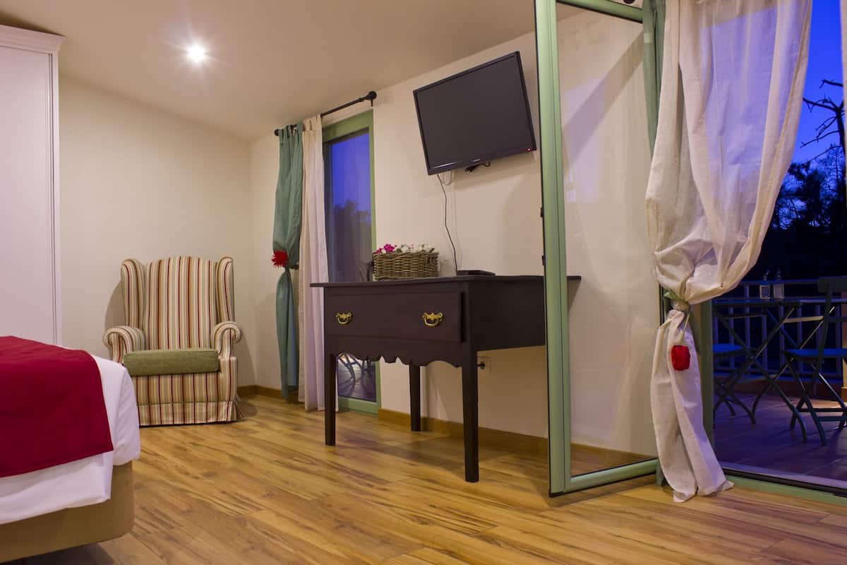 Quarto com cama, escrivaninha, cadeira, televisão e varanda com cadeiras.