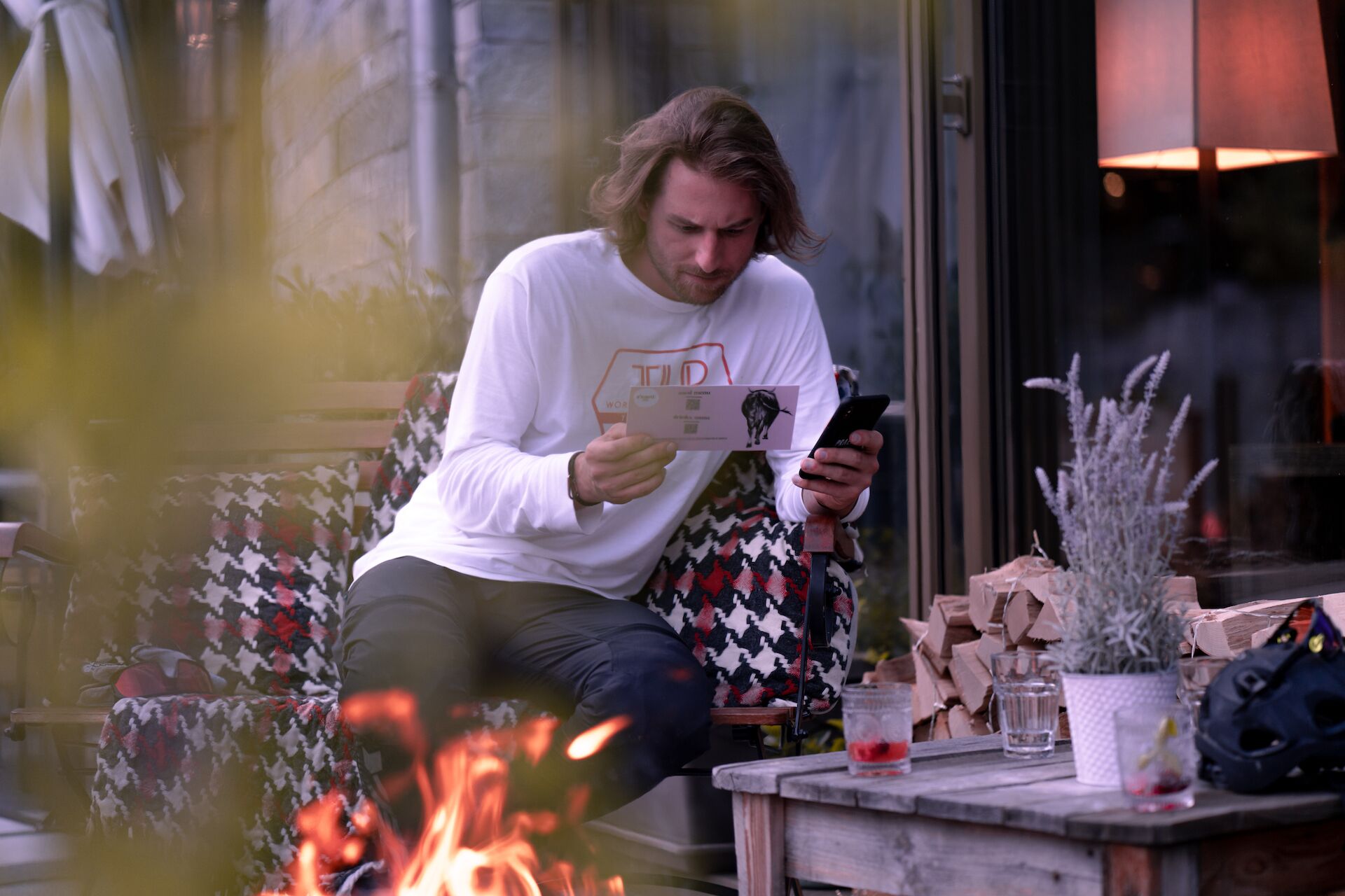 A person sitting at a table with a smartphone, a card, and a small plant.