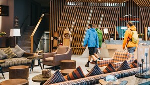 A modern interior with a high ceiling, wooden slats, and a central seating area with sofas and armchairs. - Peaks Place (Laax)
