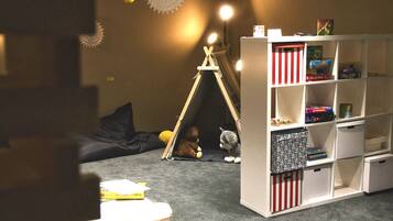 Cozy playroom with a seating area, play tent, and bookshelf filled with children's books and toys.