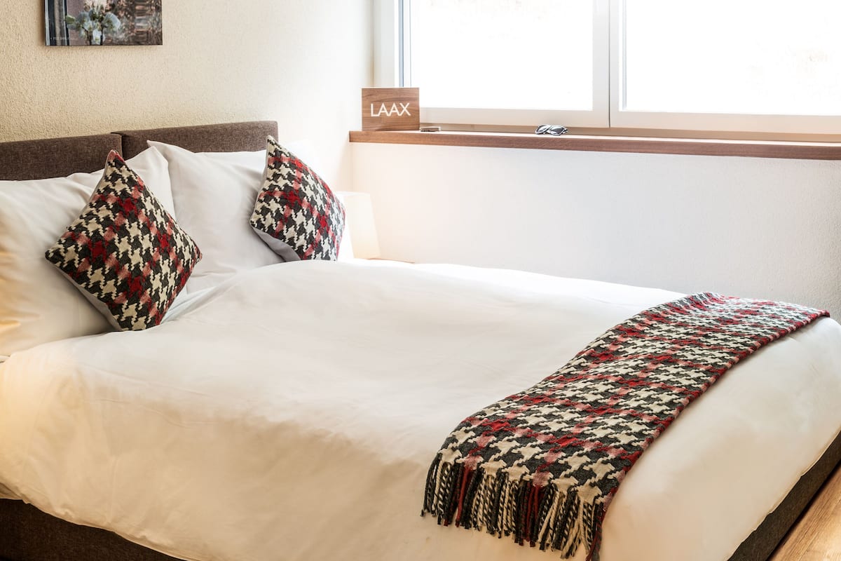 A neatly made bed with white linens, two patterned pillows, and a woven throw blanket.
