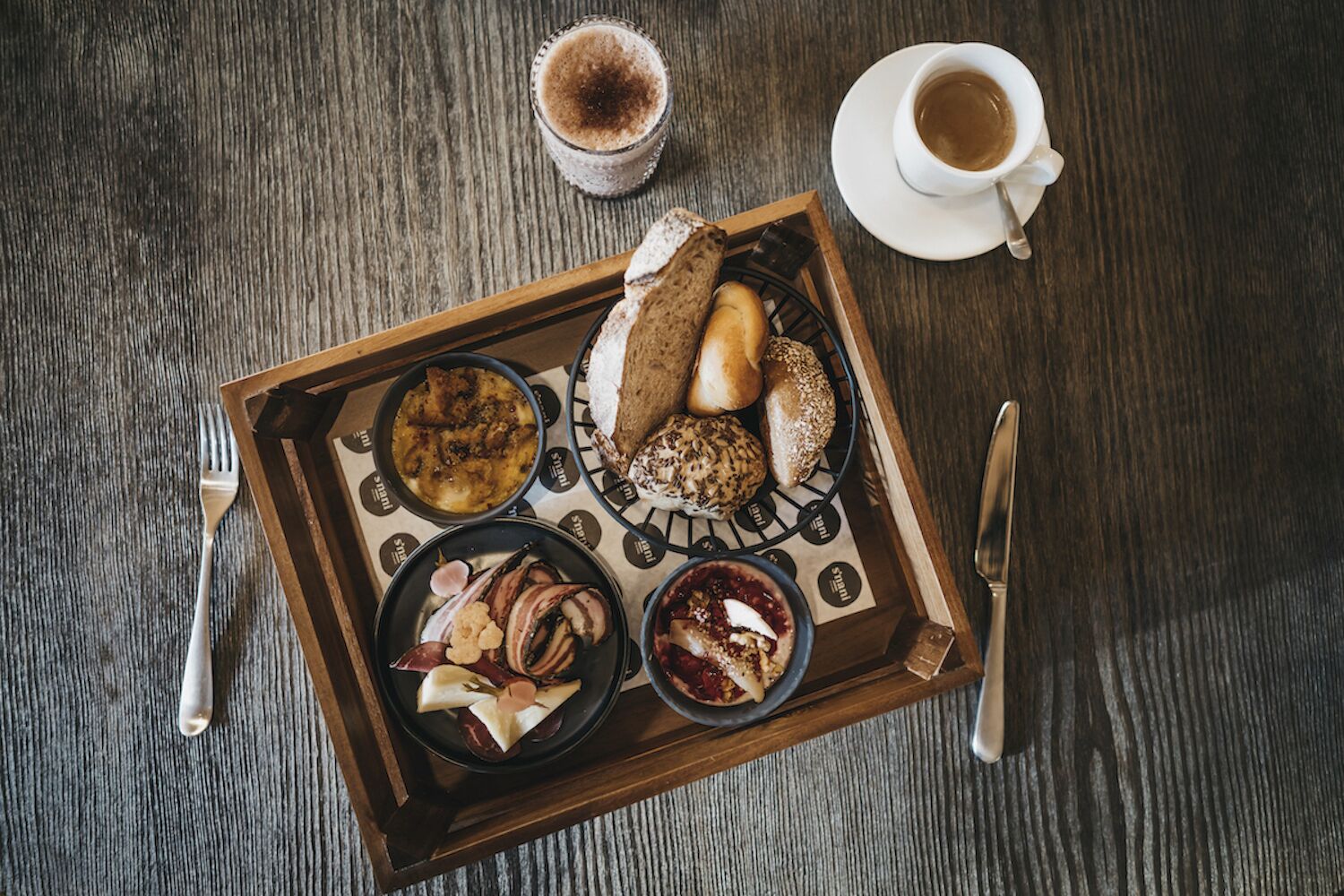 Een dienblad met verschillende etenswaren en een kop koffie op een houten tafel.