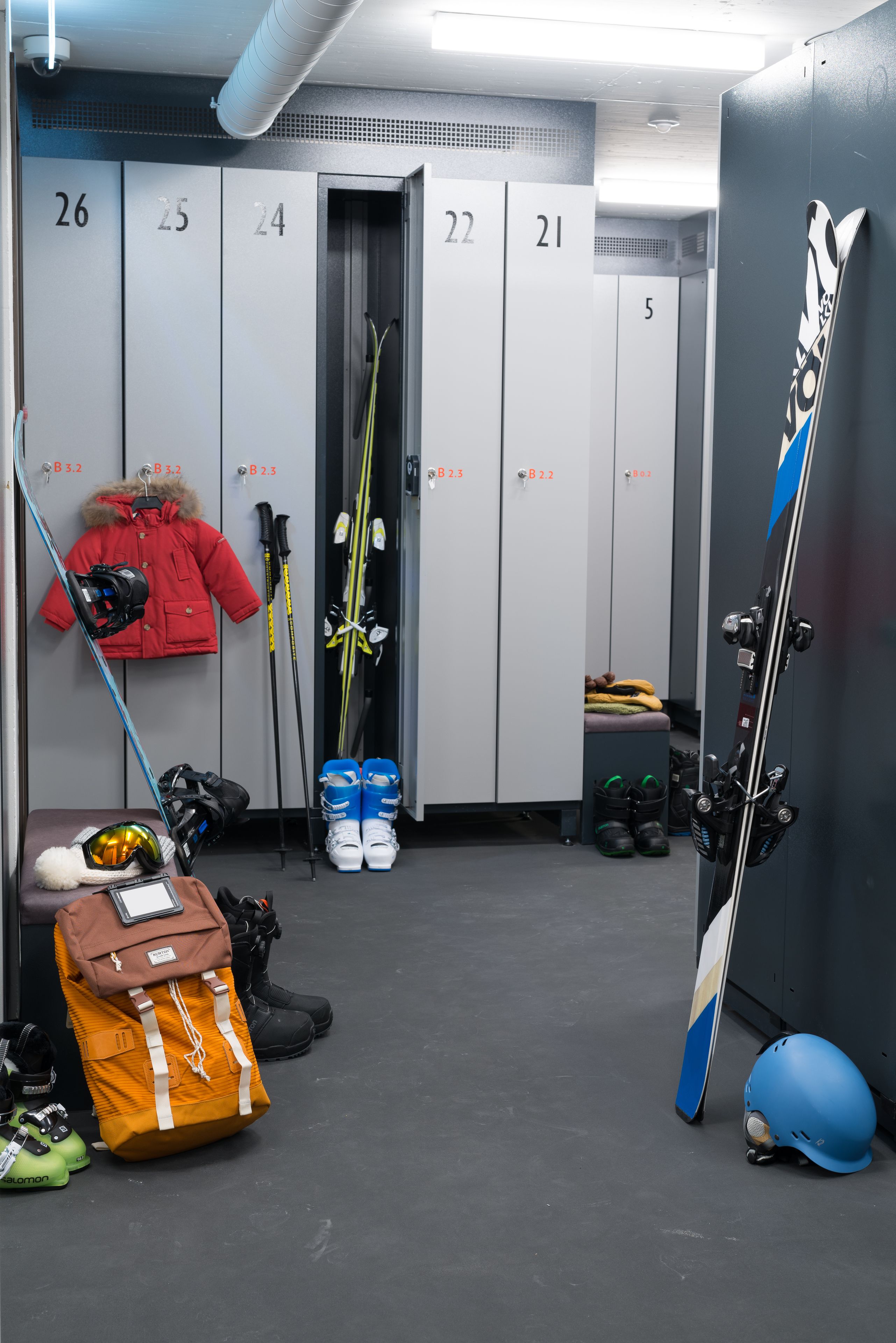 A locker room with numbered lockers, skis, ski poles, and a helmet.