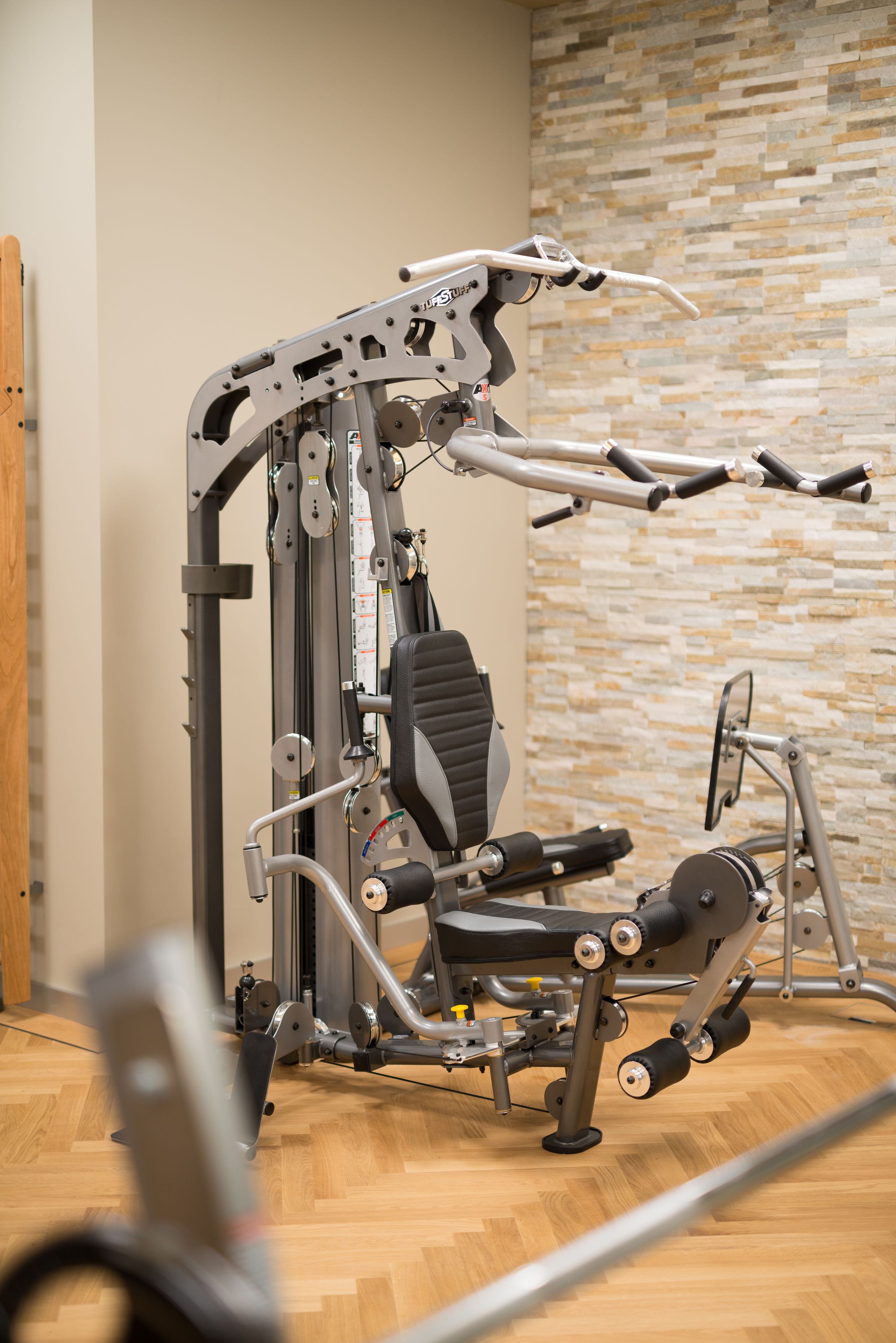 A gym with a weight machine, a wall with a mosaic pattern, and a wooden floor.