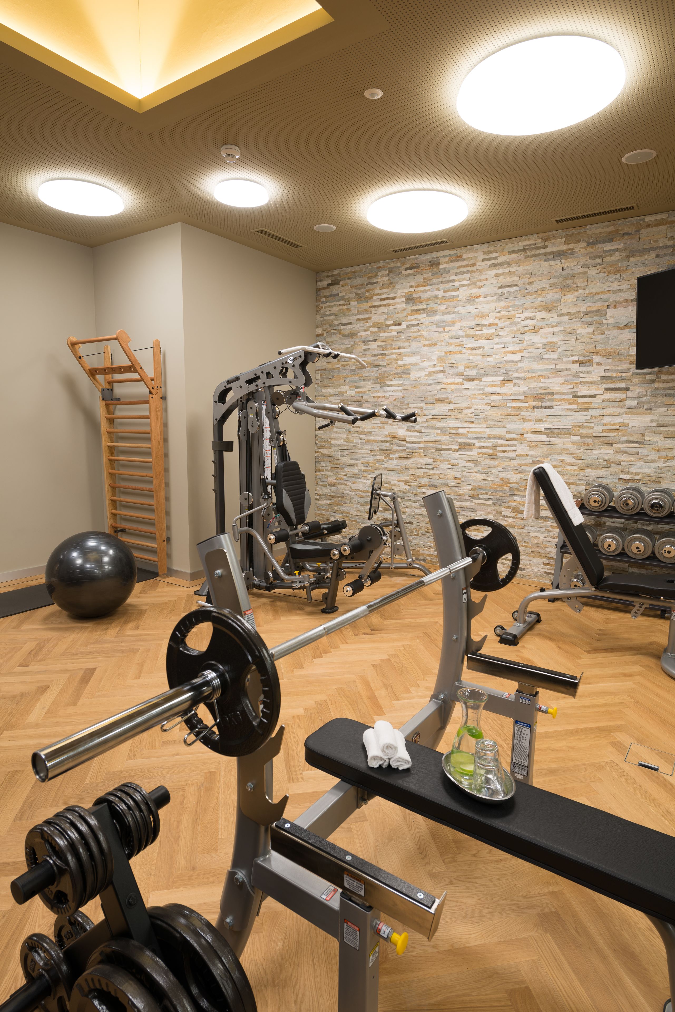 Ein Fitnessraum mit Trainingsgeräten, Holzboden und einer Steinwand.