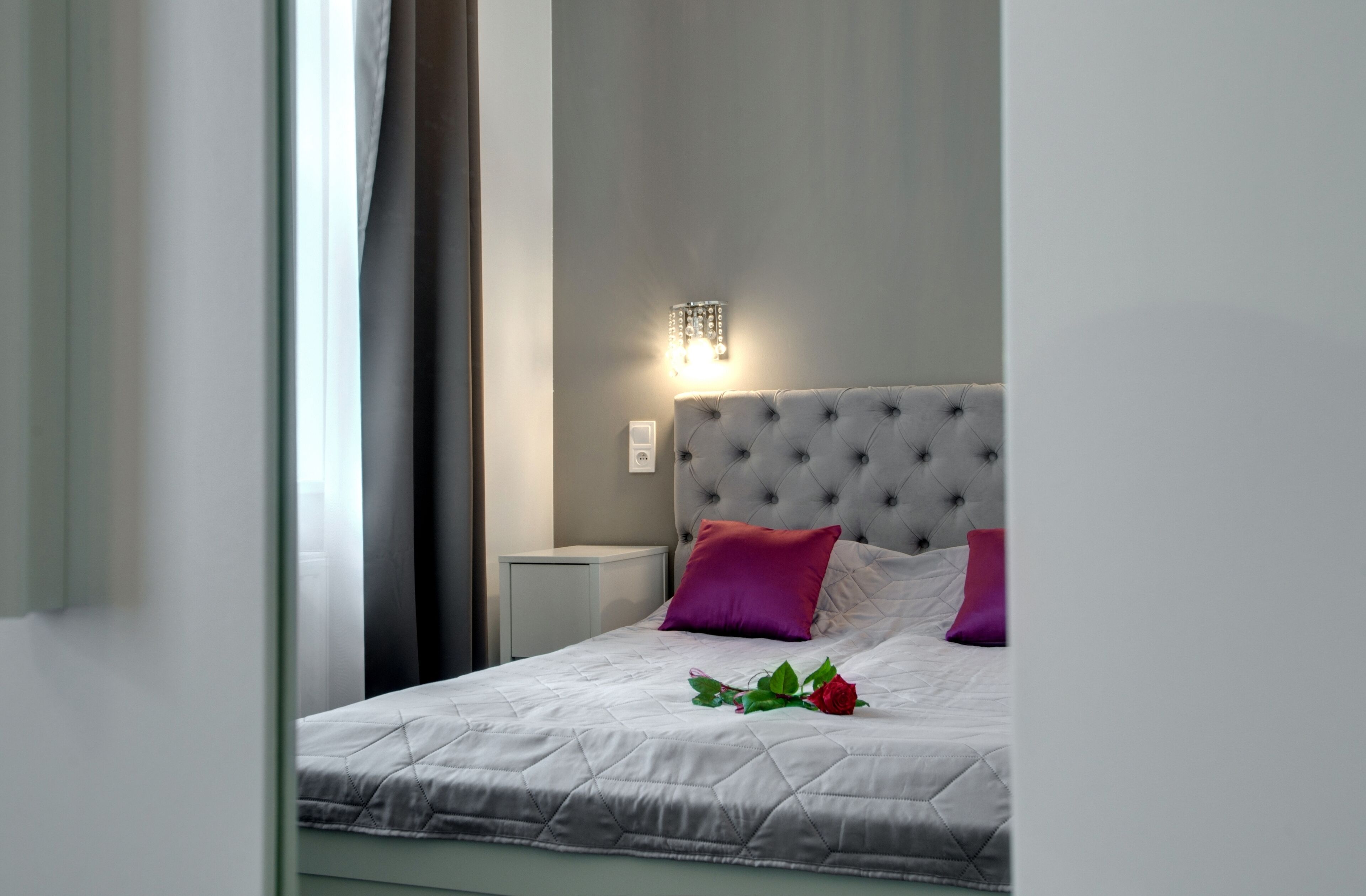 Una cama bien hecha con cubrecama acolchado, dos almohadas y una rosa decorativa.