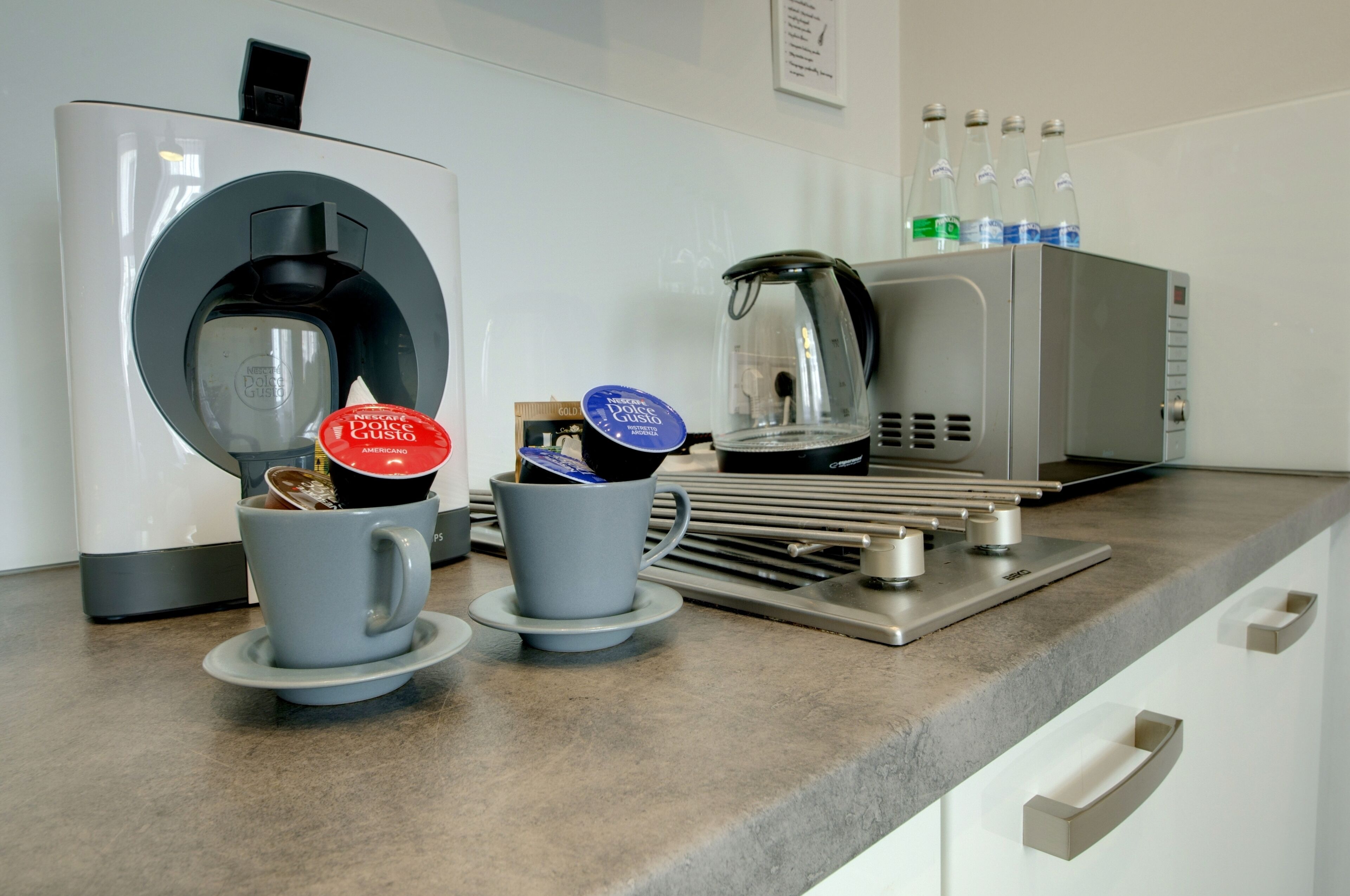 Una cafetera con dos tazas de café, una tetera y un dispensador de agua sobre una encimera de cocina.