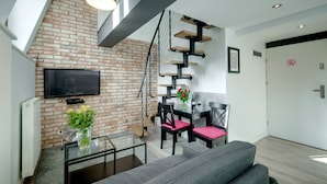 Un salon moderne avec un mur en briques, un téléviseur à écran plat, un coin repas comprenant une table et des chaises, et un escalier au design original.