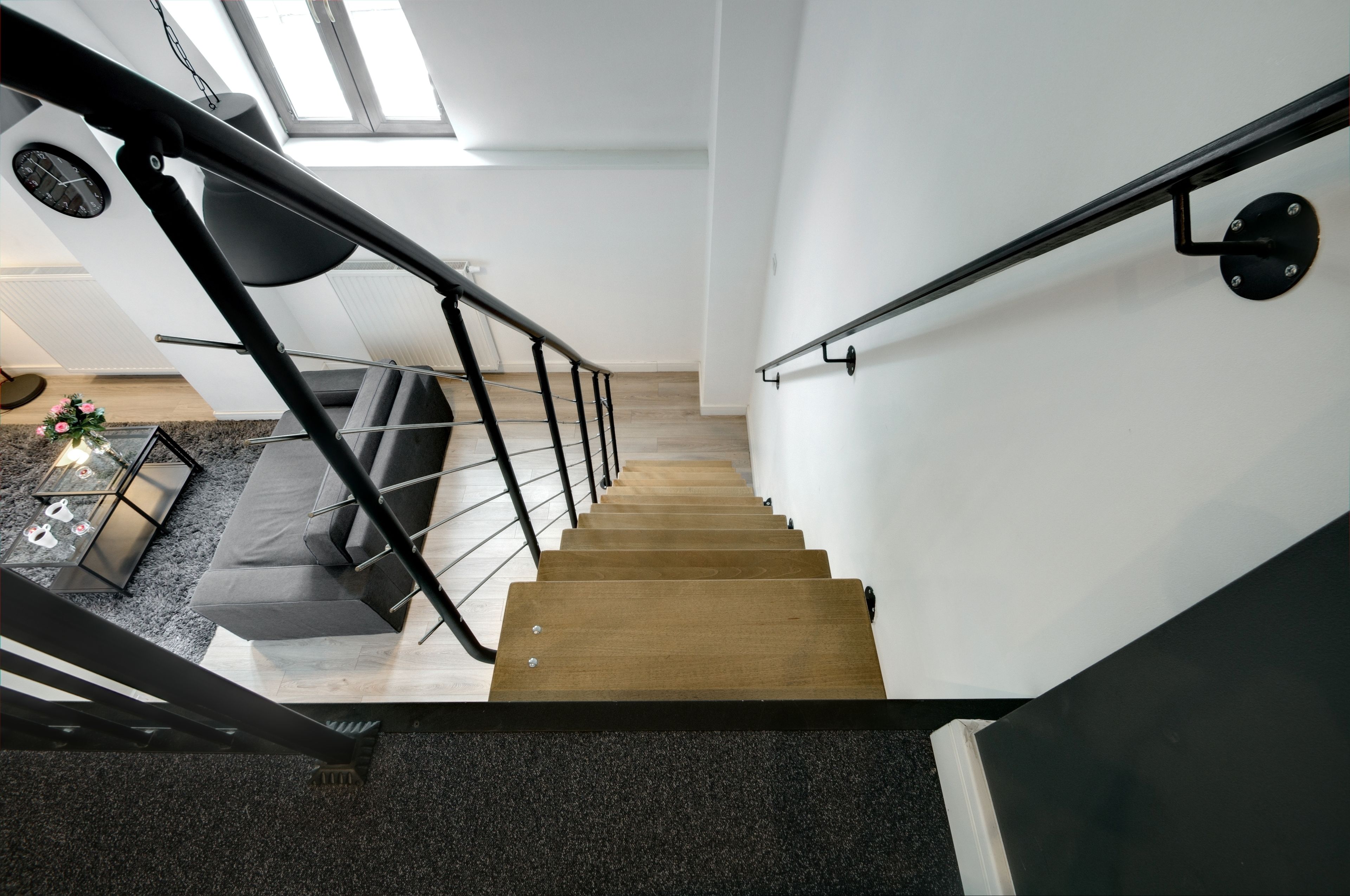 A modern staircase with a black handrail and wooden steps leading to a lower level.