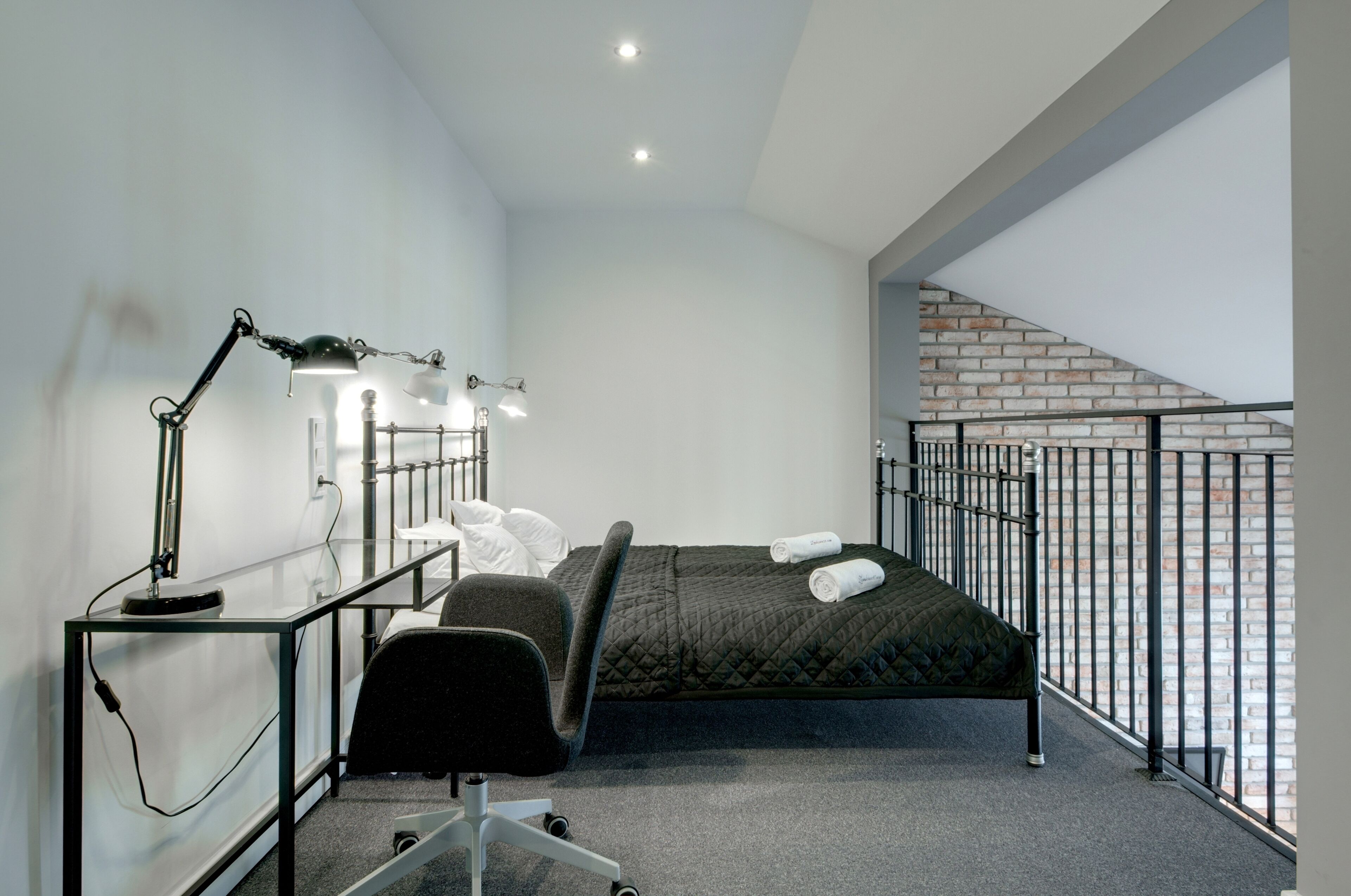 A modern bedroom with a bed, desk, chair, and a view of a brick wall.