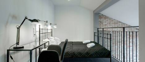 A modern bedroom with a bed, desk, chair, and a view of a brick wall.