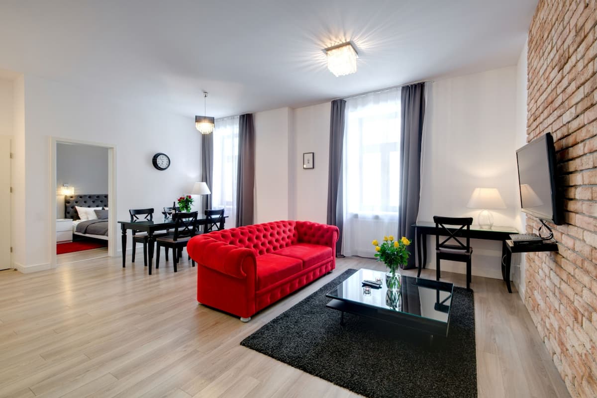Een moderne woonkamer met een rode bank, een glazen bijzettafeltje, een televisie en een bakstenen muur.