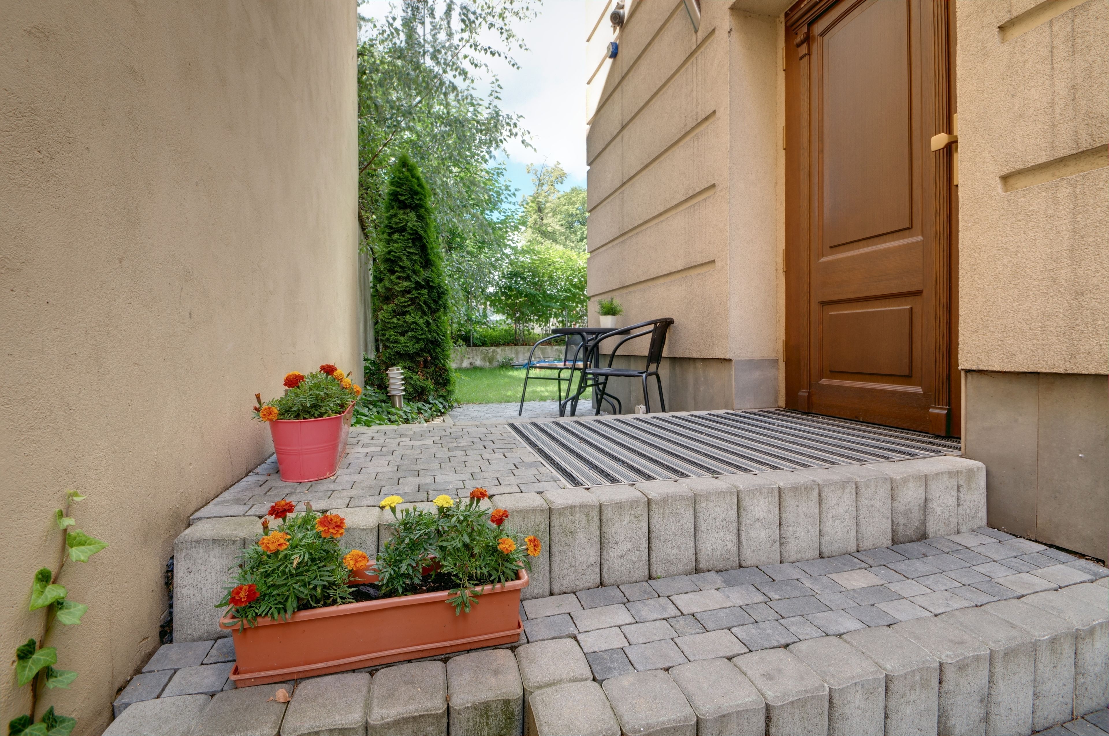 A set of concrete steps leading to a wooden door, with a small garden area featuring potted plants and a metal chair.