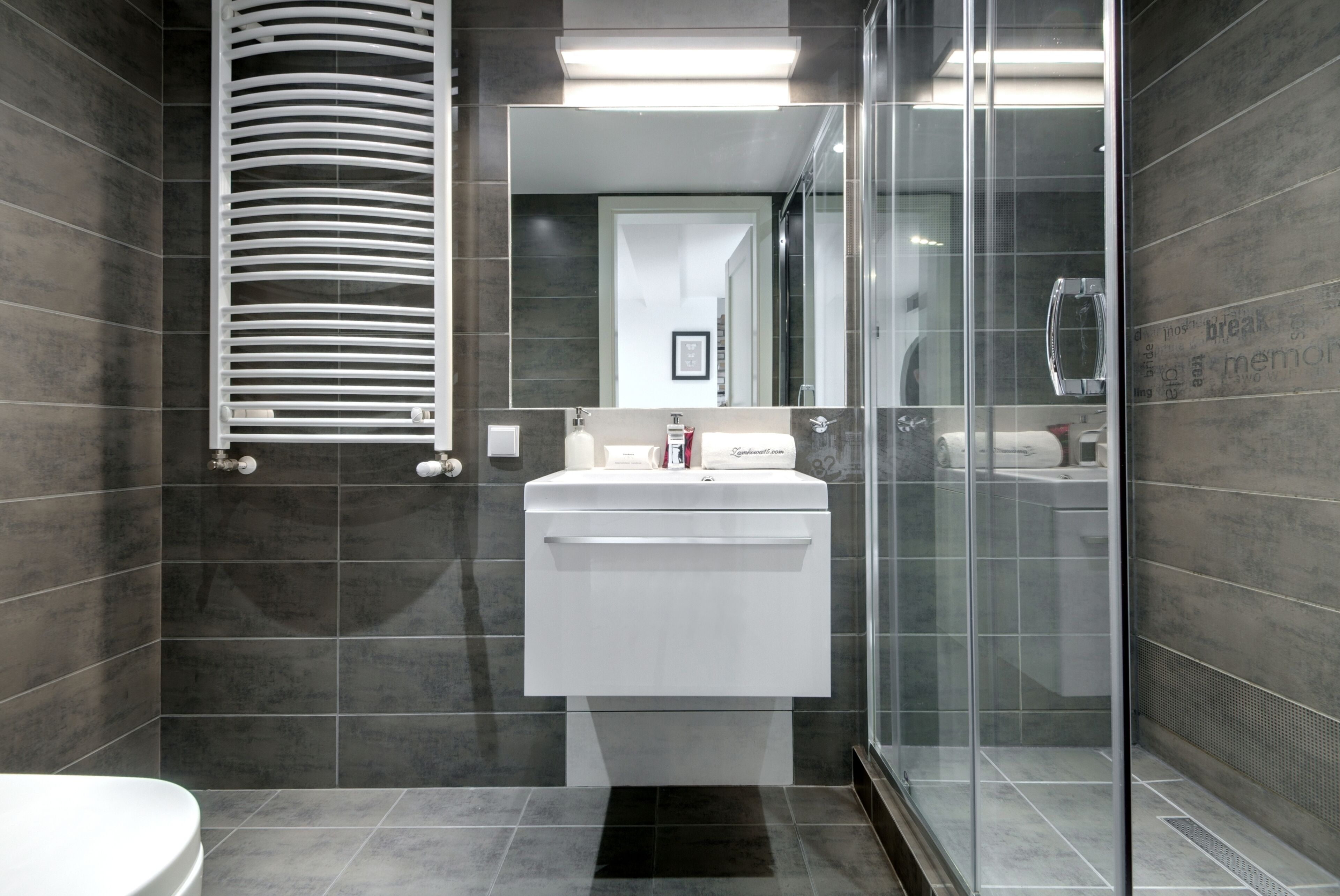 A modern bathroom with a white sink, dark tiled walls, and a glass shower enclosure.
