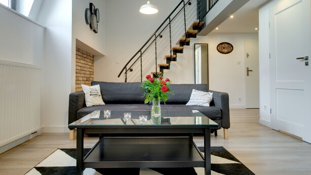 Un salon moderne avec une table basse en verre, un canapé gris et un escalier avec des marches en bois.