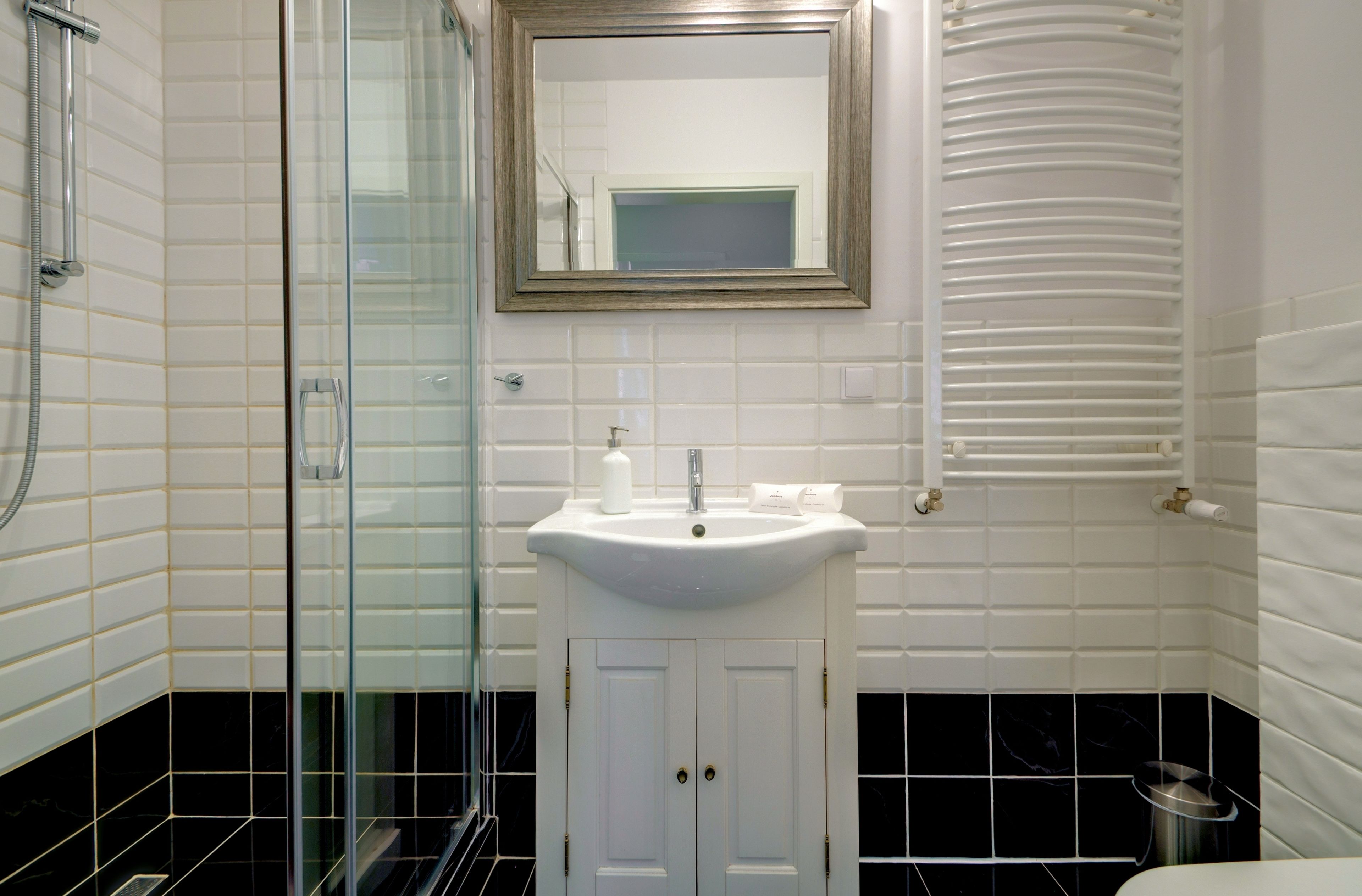 A bathroom with a glass shower enclosure, a white sink with a mirror above it, and a towel rack.