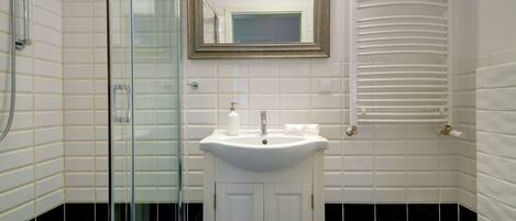 A bathroom with a glass shower enclosure, a white sink with a mirror above it, and a towel rack.