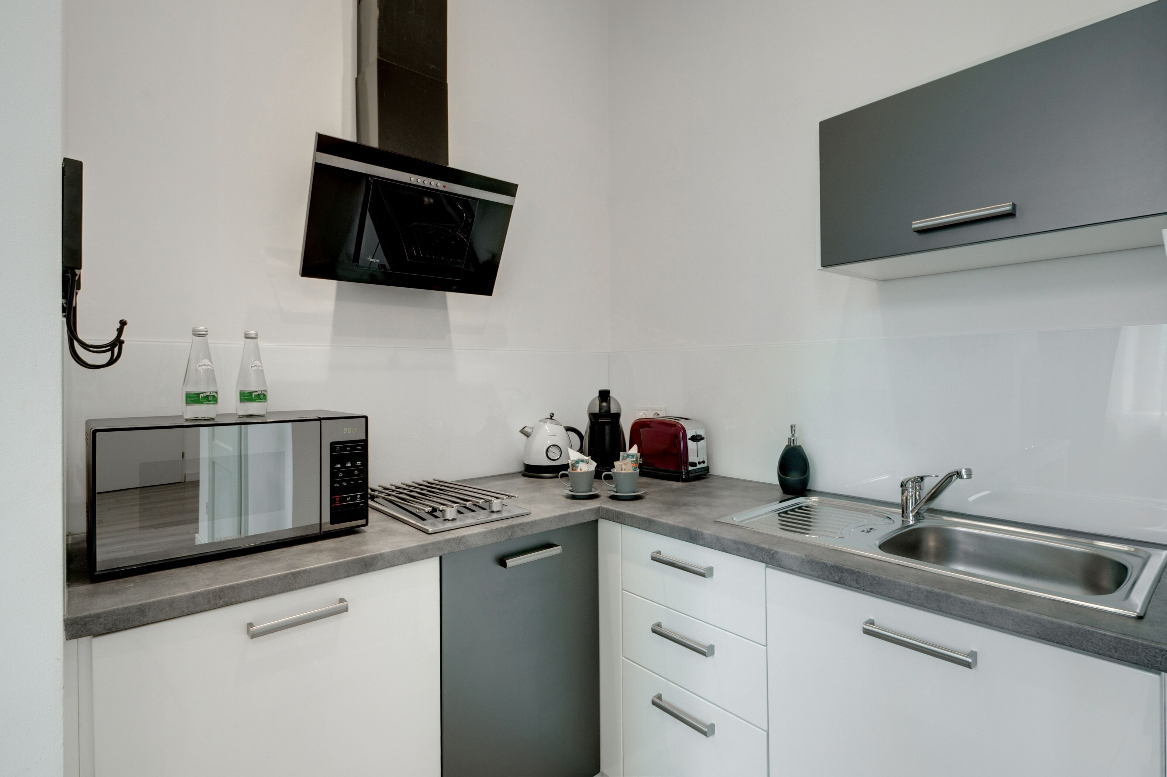 A modern kitchen with a built-in microwave, kettle, toaster, and a stainless steel sink.