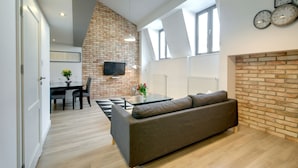 Un salon moderne avec un canapé en cuir marron, un coin repas doté d’une table à carreaux noirs et blancs, et un mur d’accent en briques.