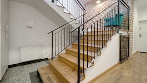Un escalier avec des marches en bois et des rampes noires, menant à une pièce dont un mur est en briques et qui contient un fauteuil de couleur turquoise.