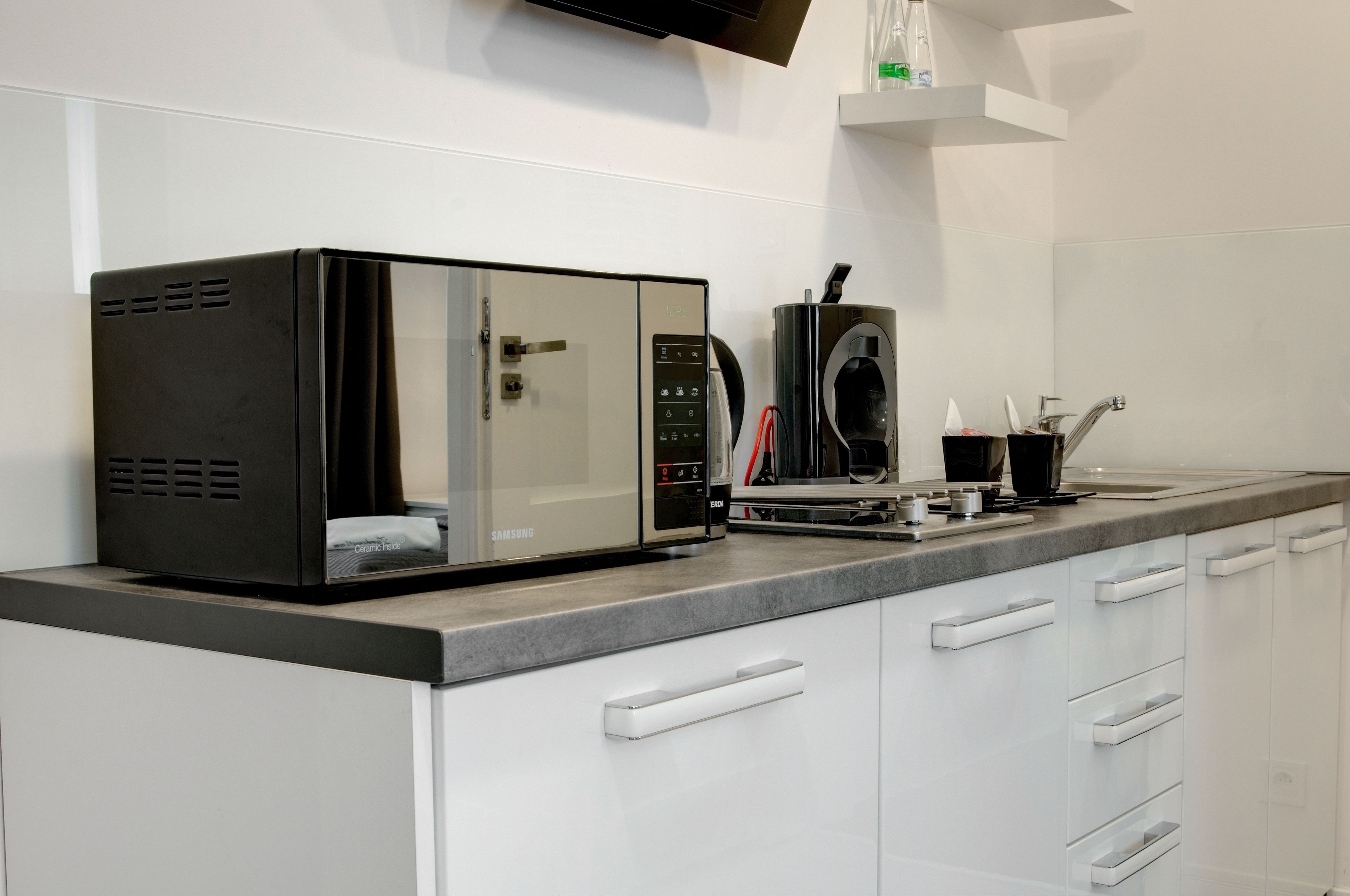 Une cuisine moderne équipée d’un four à micro-ondes encastré, d’une machine à café et d’une hotte aspirante en acier inoxydable.