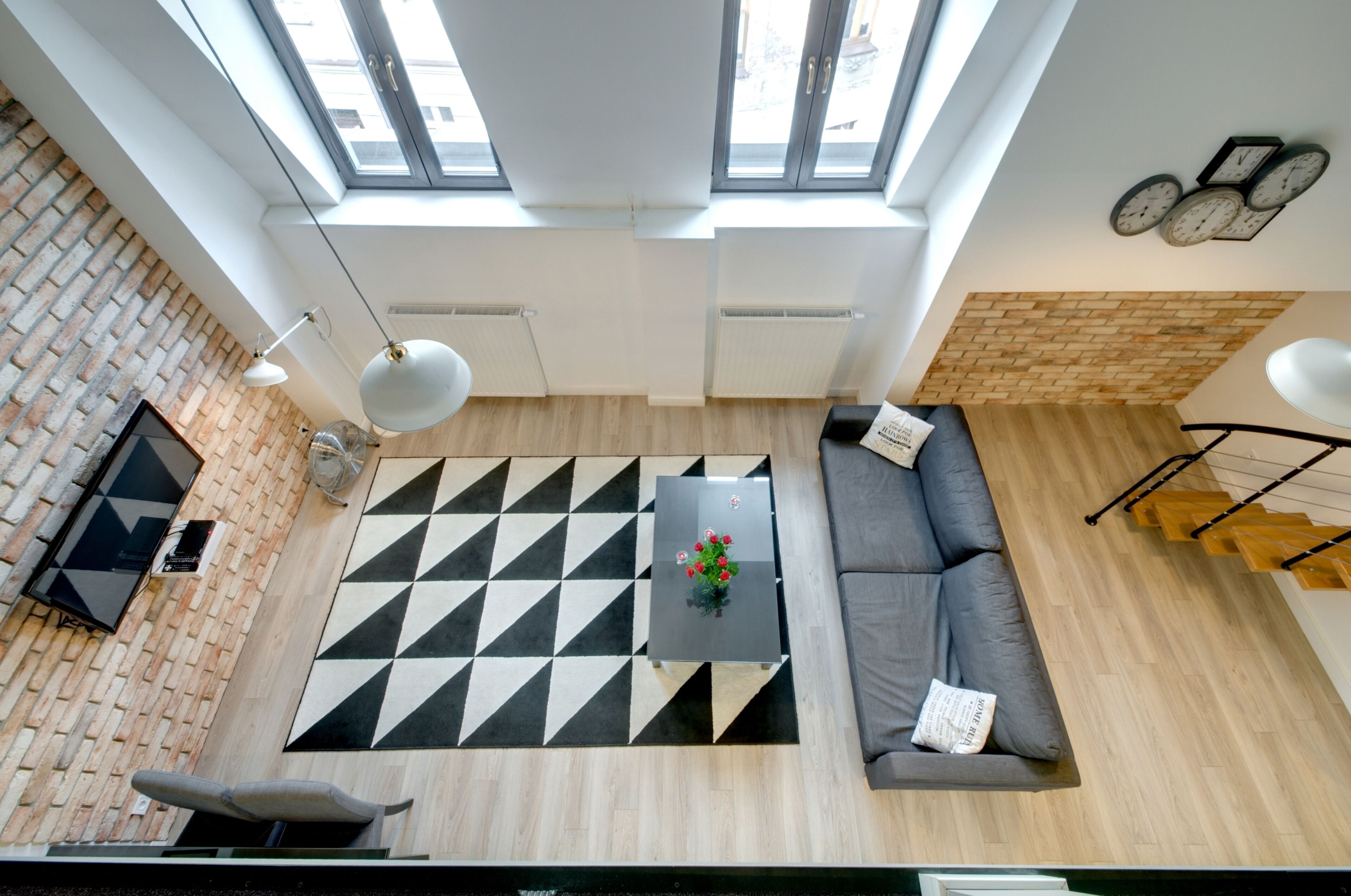 A modern living room with a black and white geometric rug, a grey sofa, and a coffee table with a vase of flowers.