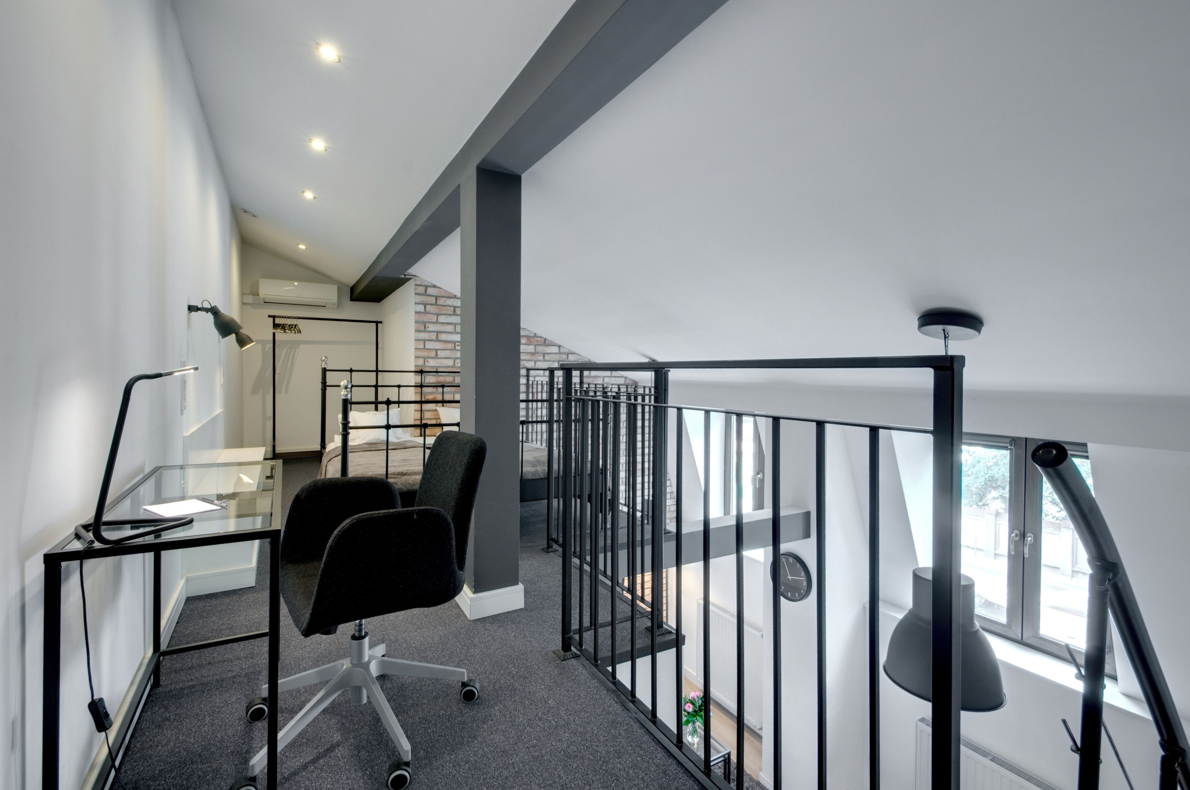 Een moderne kantoorruimte met een glazen bureau, een zwarte bureaustoel en een zwarte metalen balustrade.