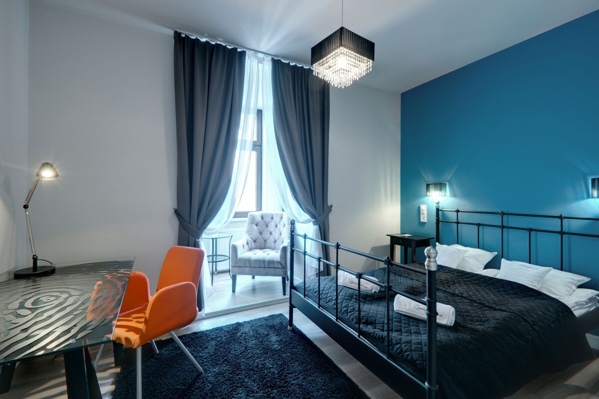 Moderni hotellihuone, jossa on suuri sänky, työpöytä tuoleineen, kattokruunu ja näkymä ulos.