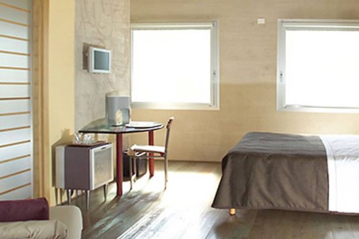 A hotel room with a bed, a desk, a chair, a TV, and a wardrobe.