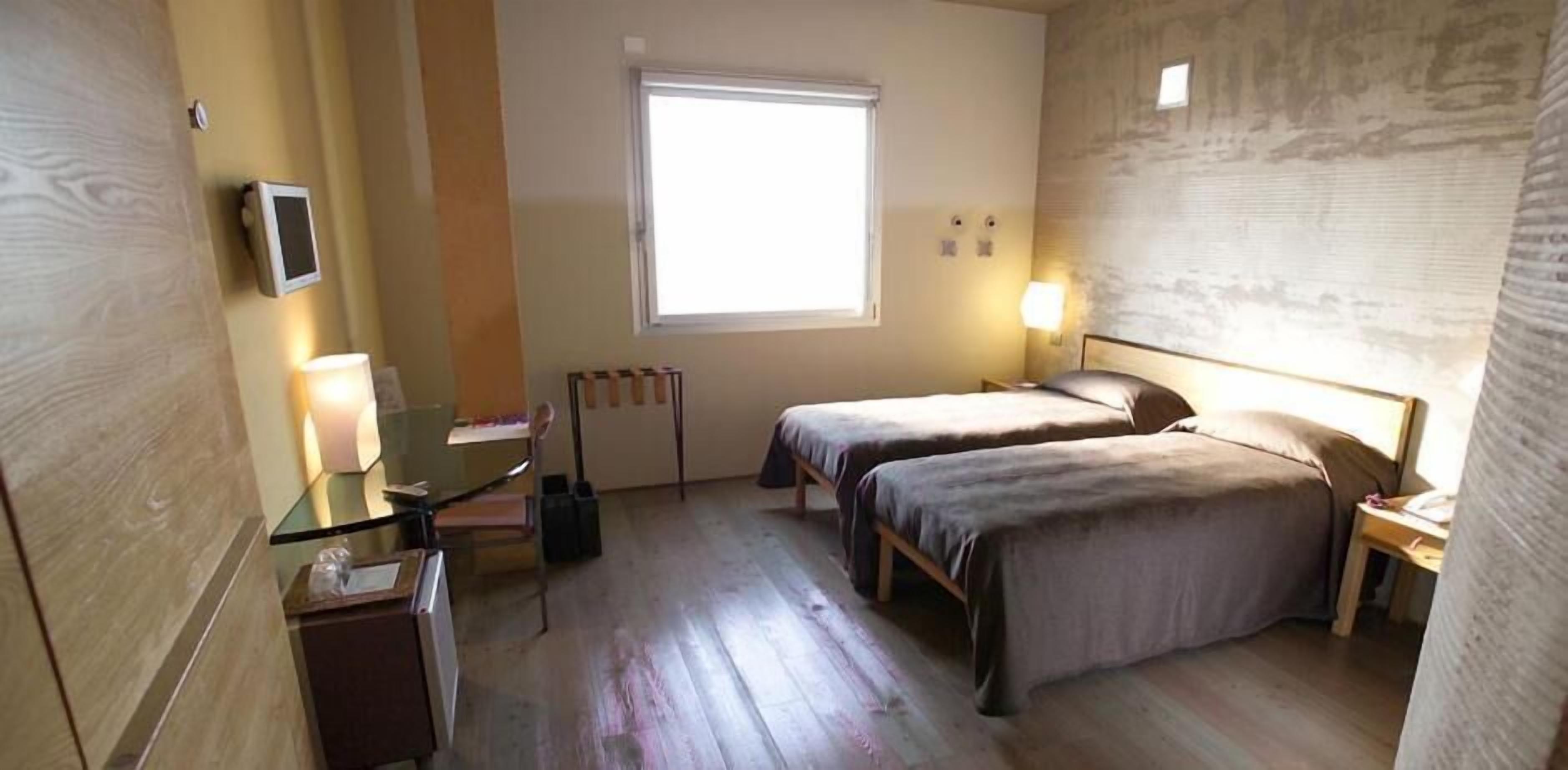 Ein Hotelzimmer mit zwei Betten, einem kleinen Schreibtisch, einem Stuhl, einem Fenster und einer Heizung.