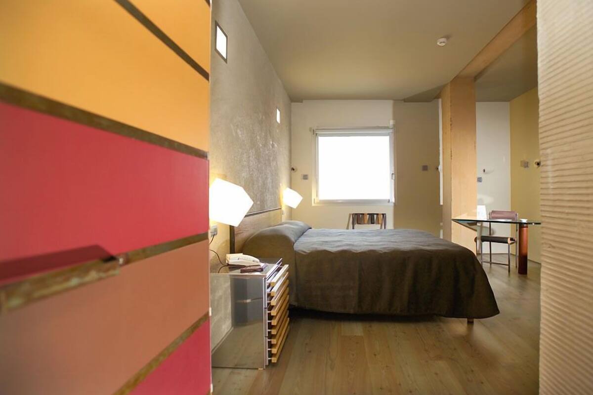 A bedroom with a bed, bedside table, lamp, and a window.
