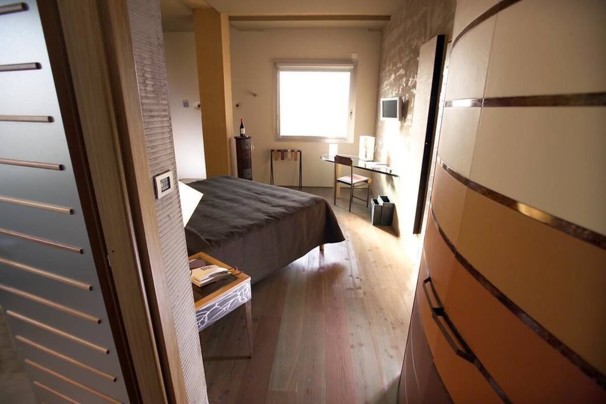 A bedroom with a bed, a desk, and a chair. There is a window providing natural light.