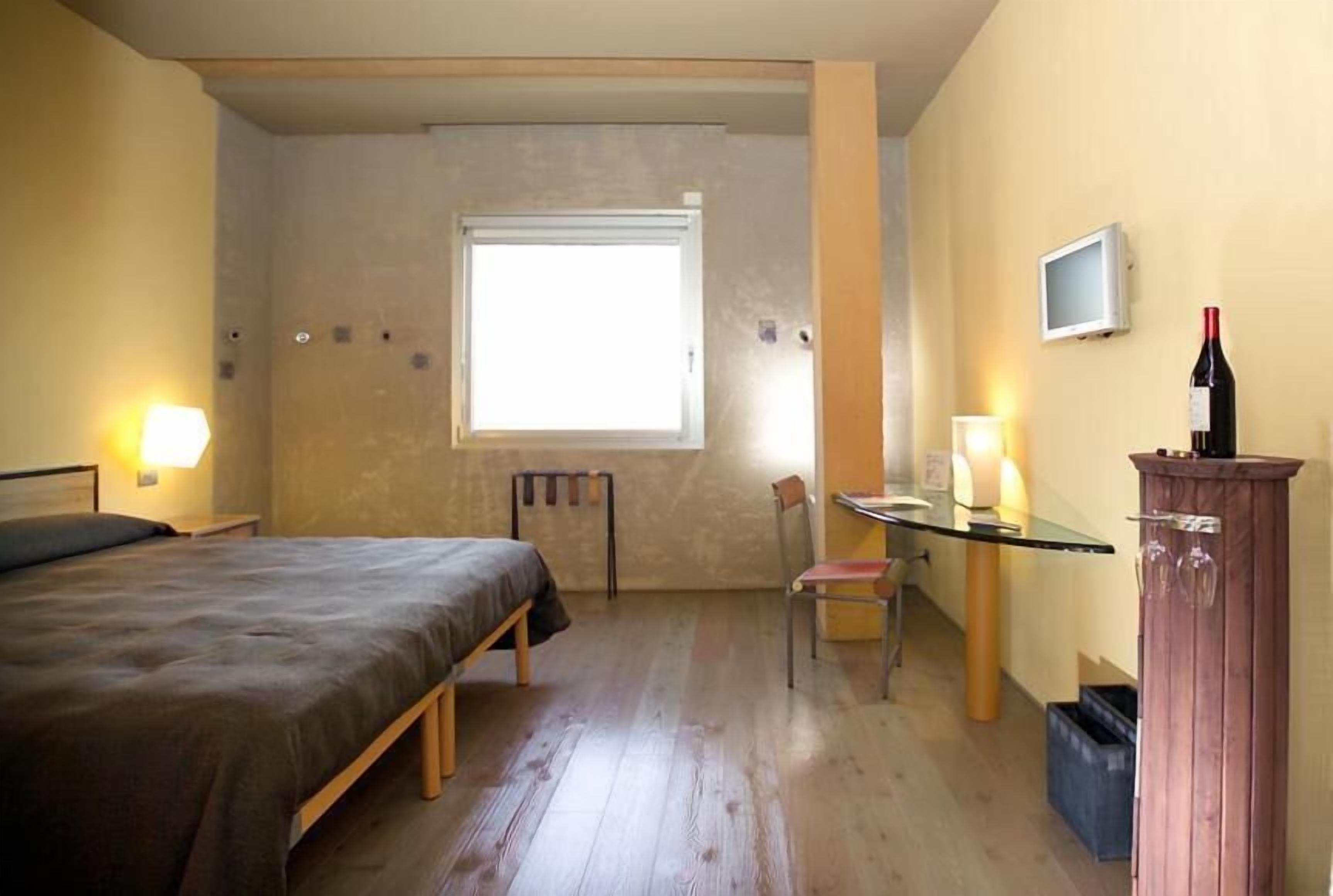 Ein Schlafzimmer mit einem Bett, einem Schreibtisch, einem Stuhl, einem Fernseher und einer Weinflasche.