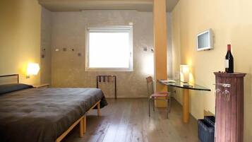 A bedroom with a bed, a desk, a chair, a television, and a wine bottle.