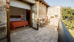 Habitación de paredes de piedra con cama, una mesa y sillas, y un pequeño balcón.