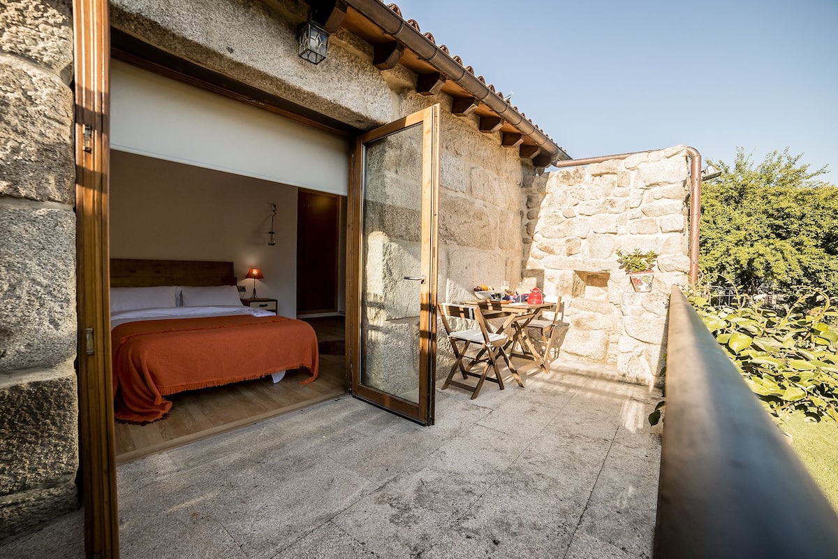 A stone-walled room with a bed, a table with chairs, and a small balcony area.