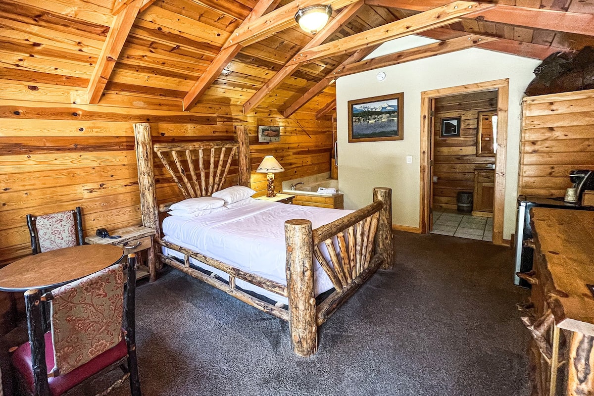 A log cabin bedroom with a bed, a chair, a table, and a wooden ceiling.