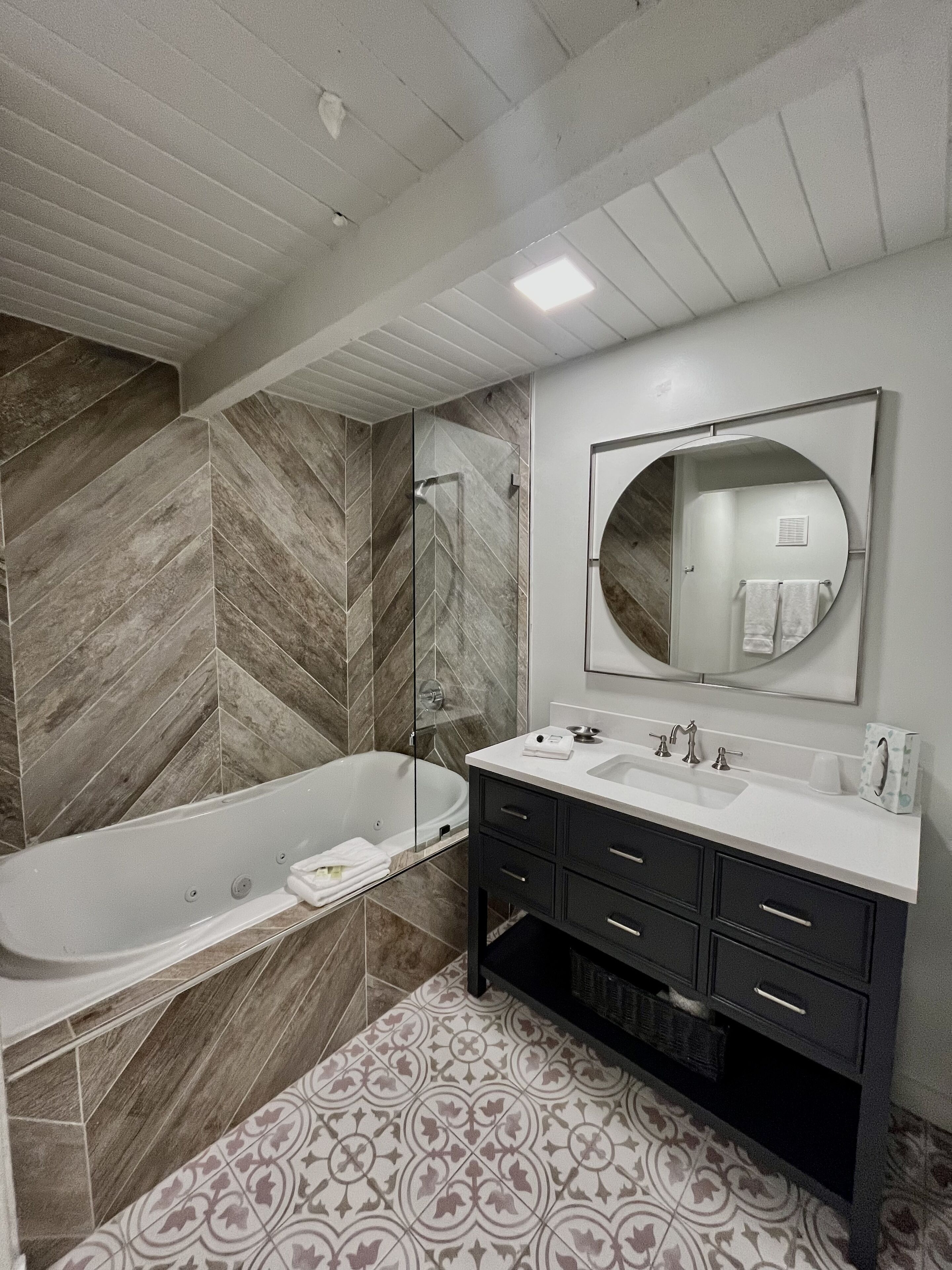 A modern bathroom with a freestanding bathtub, a large mirror, and a vanity with a sink and multiple drawers.
