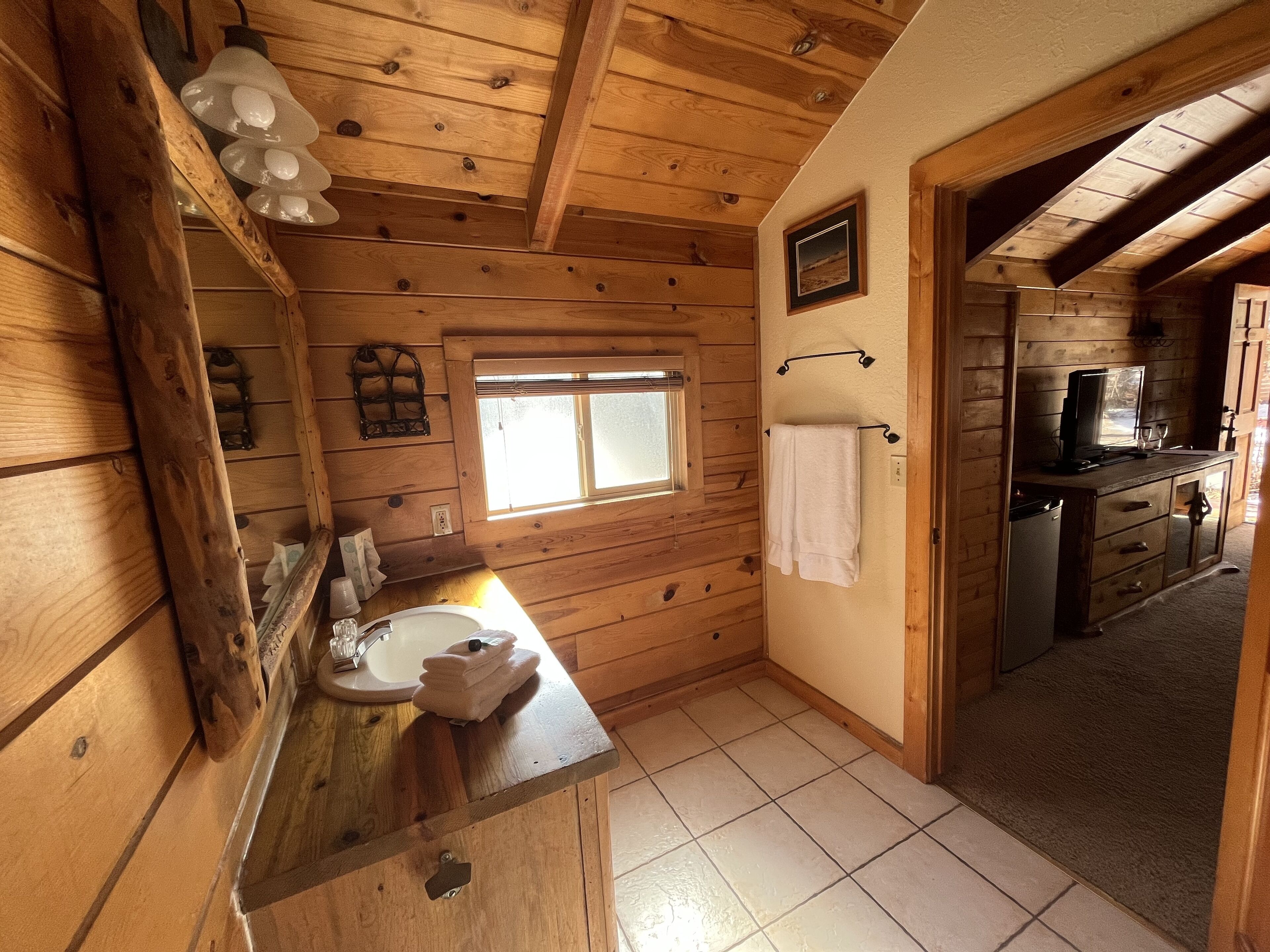 L’intérieur d’une cabane en bois, avec un plafond en bois, une fenêtre, un évier, un porte-serviettes et un petit coin cuisine.