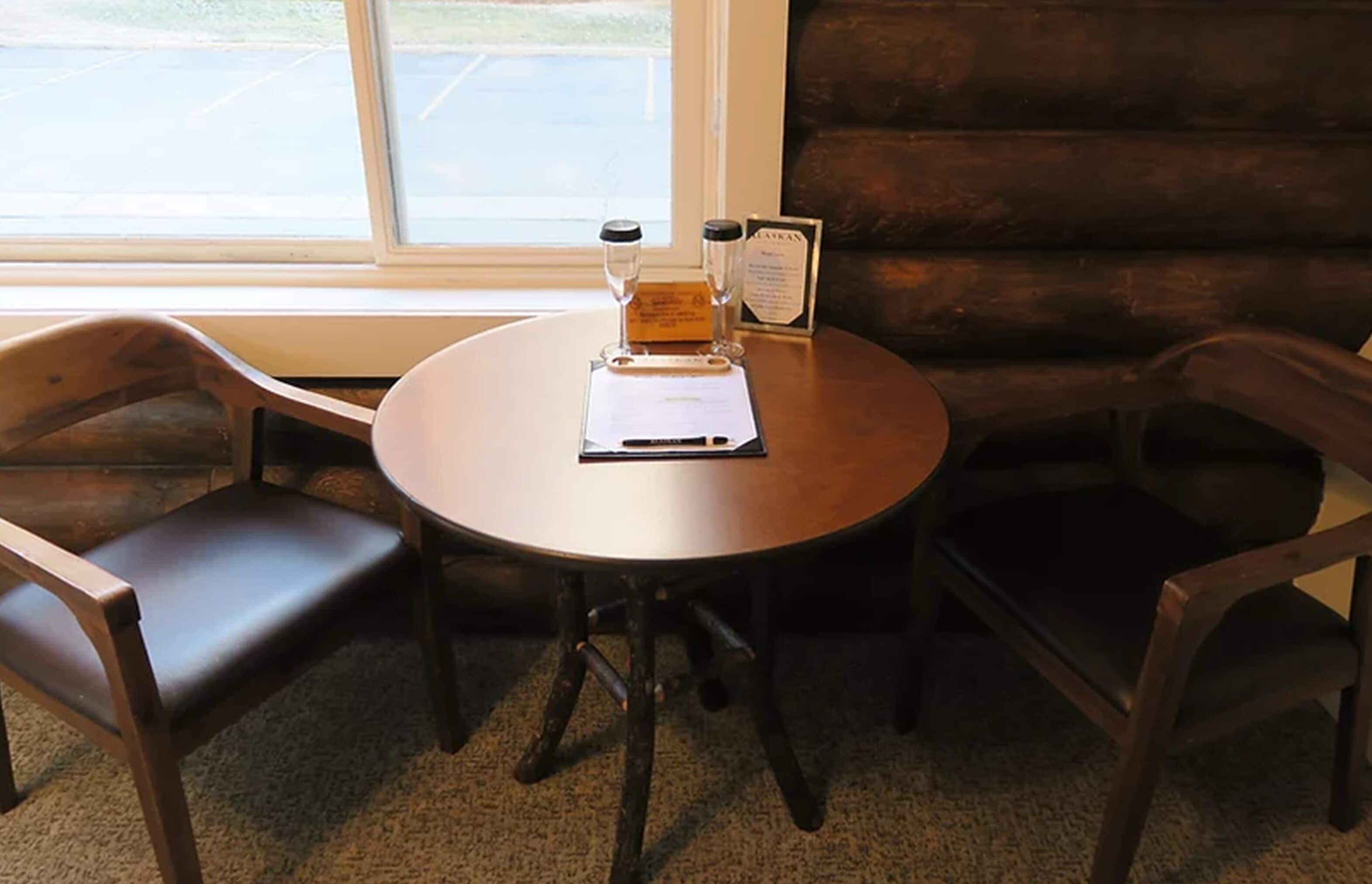 A round wooden table with a menu and two salt and pepper shakers, surrounded by two dark wooden chairs.