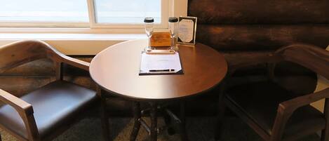 A round wooden table with a menu and two salt and pepper shakers, surrounded by two dark wooden chairs.