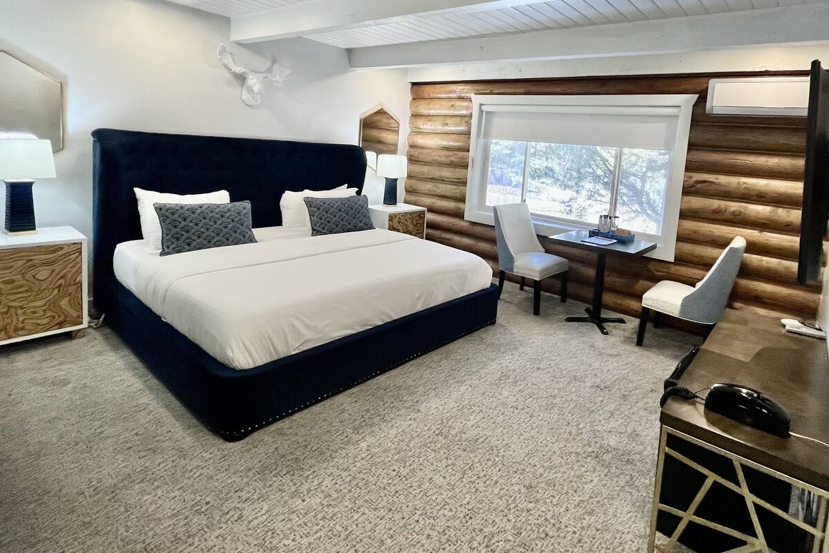 A bedroom with a large bed, two chairs, a desk, and a window.