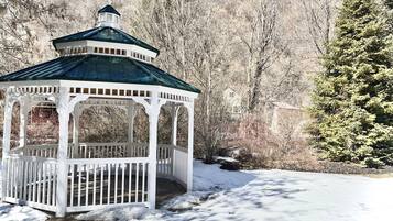 Un kiosque blanc avec un toit vert, entouré de neige et d’arbres.